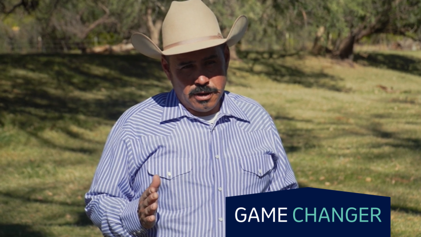 A man in a cowboy hat stands in a pasture.