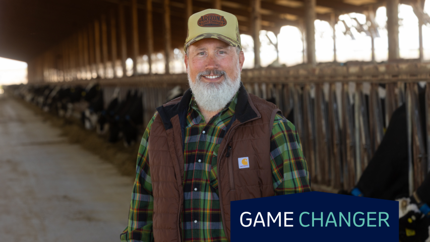 A man in a hat and vest stands in front of a cattle feeding bunk.