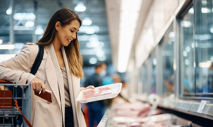 woman at the grocery store looking at a package of steaks. 